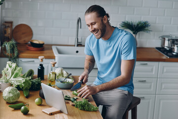 Happy young man looking at digital tablet while preparing food at the domestic kitchen