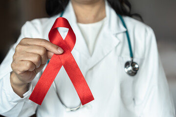 World aids day and national HIV AIDS and ageing awareness month with red ribbon on medical or surgical doctor's hand - obrazy, fototapety, plakaty