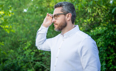 Handsome businessman looking aside in eyeglasses natural background, copy space