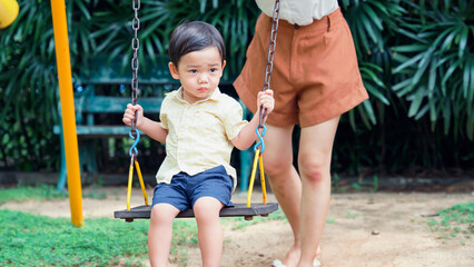 Cute little Asian boy is playing on a swing in the playground.