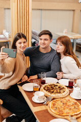 A group of friends is having pizza in a cozy restaurant and taking selfies, taking pictures together. A cheerful group of friends.