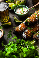 Grilled corn cobs with fresh herbs,lime,beer and salt, served on stone table.