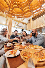 A cheerful group of friends is eating delicious pizza in a restaurant. Friends are sitting in a restaurant and having fun.