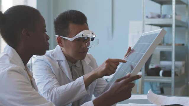 From above shot of diverse team of lab engineers examining drawing plans and technical schemes while coworking on environmental project sitting at office desk with solar panel on it