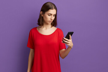 I'm tired of this gadgets. Pensive young pretty brunette girl in red t-shirt using smartphone...