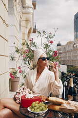 Attractive woman in bathrobe enjoying champagne while having brunch on the balcony