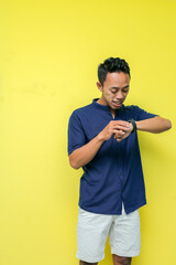 man in blue shirt and white pants looking at his watch, on a yellow background
