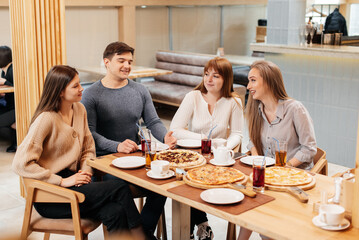 A group of friends is having pizza in a cozy restaurant. Meeting friends over dinner, socializing with a friendly company.
