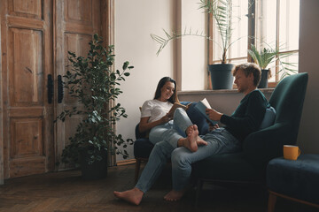 Beautiful young couple reading books while relaxing at home together