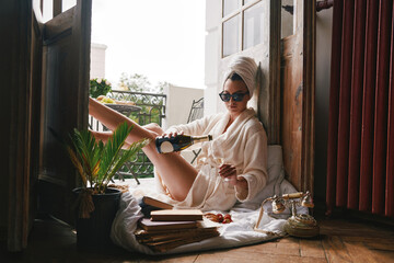 Attractive young woman in bathrobe pouring some champagne while relaxing on the balcony