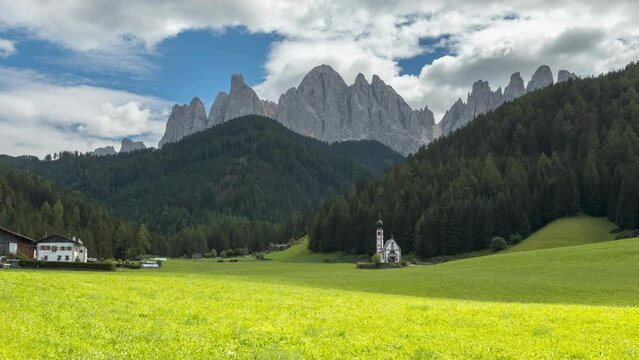 Timelapse of the Italian Dolomites with the Church of St. Johann in Ranui, dramatic mountain peaks, green alpine meadow and moving clouds in South Tyrol, Italy