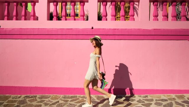 woman in White dress dancing on the street. Joyful african girl in summer dress turning around. stylish girl traveler in a dress holds the flag of south africa and has fun near the colored houses