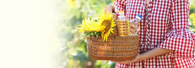 Woman holding basket with bottles of oil and sunflowers in field. Banner for design
