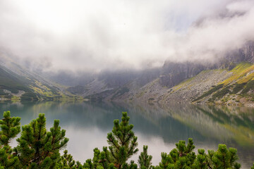Mountain in the Polish Tatras with a small turquoise lake and rocks in the middle of the mountain with white fog and clouds