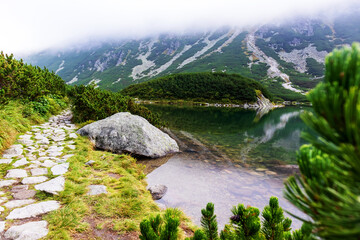 Fototapeta na wymiar A very impressive view of the Polish Tatra mountains with many rocks with a incredibly beautiful turquoise lake in the middle of mountains with the reflection of white clouds and mountains