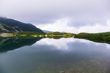 A very impressive view of the Polish Tatra mountains with many rocks with a incredibly beautiful turquoise lake in the middle of mountains with the reflection of white clouds