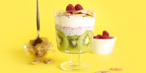 Glass of delicious chia pudding with fruits on yellow background