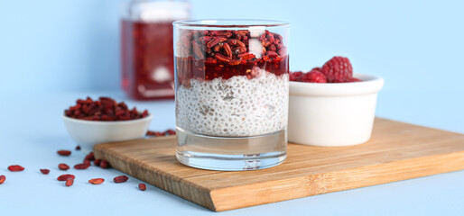 Glass of tasty chia pudding with goji berries on light blue background