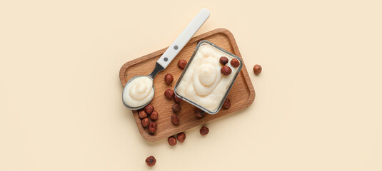 Wooden board with tasty vanilla pudding and hazelnuts on beige background, top view
