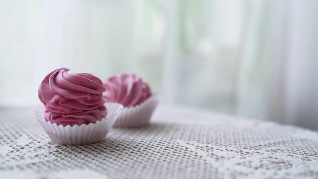 closeup hand takes two pink marshmallow cookies from small group served on table