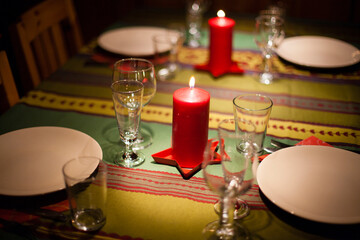 Red candles, white plates, glasses on a green tablecloth, a New Year's holiday table