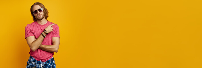 Handsome young man pointing away while standing against yellow background
