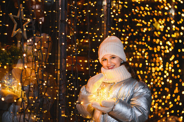 Girl and Christmas garland. Smiling girl in warm clothes at night with blurry lights. Holidays theme
