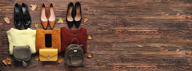 Different stylish shoes, sweaters, bags and mobile phone on wooden background with space for text. Black Friday sale