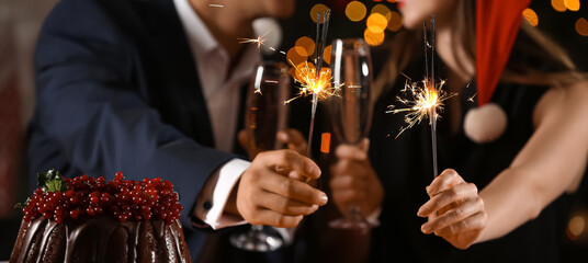 Happy young couple with sparklers and glasses of champagne celebrating Christmas at home