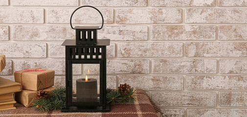 Christmas lantern with burning candle, fir branches, books and gifts on table near brick wall © Pixel-Shot