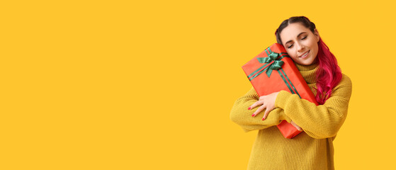 Beautiful woman holding Christmas gift box on yellow background with space for text