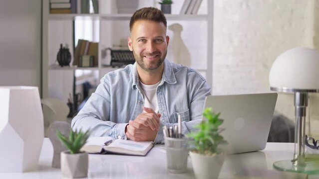 Happy businessman in casual using laptop in home office, Young adult man sitting at desk in study room, working online with computer, browsing the Internet, smiling.