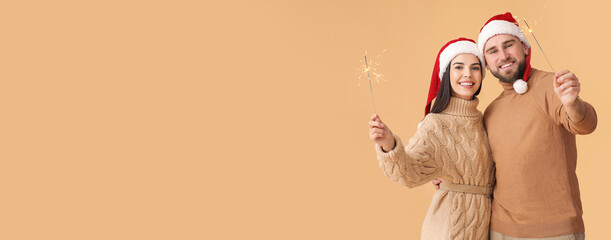 Young couple with Christmas sparklers on beige background with space for text