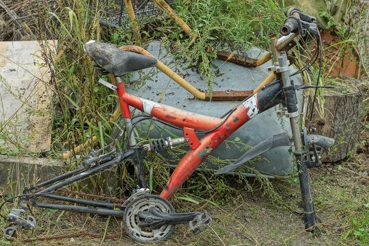 an old broken rusty red sports bike without wheels lies on the ground in a junkyard on the street