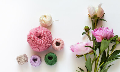 Obraz na płótnie Canvas Knitting as hobby and leisure. Skeins of cotton and wool yarn for hand knitting and crochet on a white background next to a bouquet of fresh pink peonies. Flat lay, copy space, mock up, top view