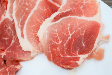 High Angle View Of Slised Meat In White Plate On Table. Fresh steak in plate. Uncooked raw pork meat slices on a white plate and wooden table.