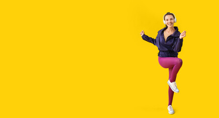 Young woman with headphones doing aerobics on yellow background with space for text
