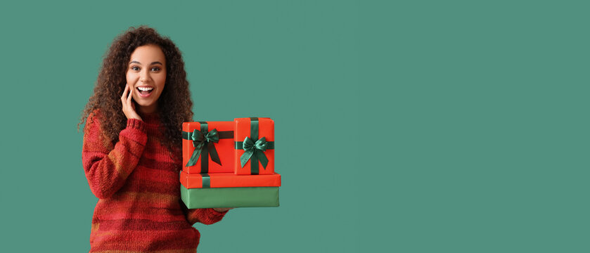 Happy young African-American woman in warm sweater holding Christmas gifts on green background with space for text