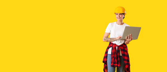 Female construction worker in hardhat using laptop on yellow background with space for text