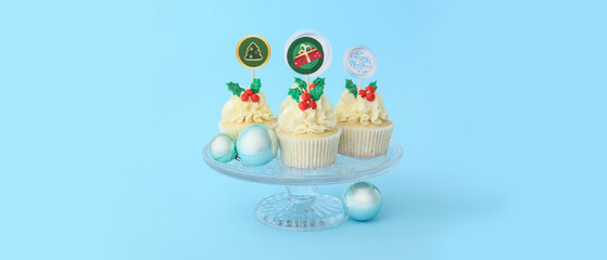 Dessert stand with tasty Christmas cupcakes on blue background with space for text
