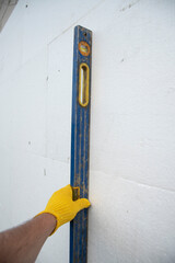thermal insulation house. Worker hand with level measuring white rigid polyurethane foam sheet on...