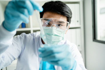 Male scientist working in a lab with blue test tubes. Asian male scientist researcher in the...