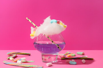 Glass with tasty cotton candy cocktail and sweets on pink background