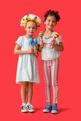 Little Mexican girls with floral wreaths and maracas on red background