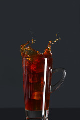 Glass cup of delicious iced coffee with splashes on dark background