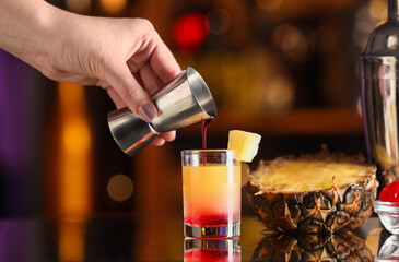 Fototapeta na wymiar Bartender pouring tasty Pineapple Upside Down Cake cocktail into glass on table
