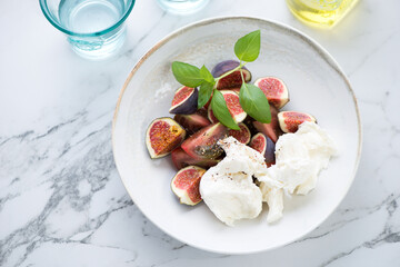 Salad with tomatoes, fresh fig fruits and mozzarella on a white marble background, horizontal shot, high angle view
