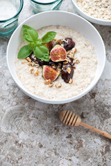 Bowl of oatmeal with figs, dates, chopped walnuts and honey on a light-brown granite background, vertical shot, elevated view