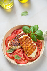 Slices of grilled halloumi cheese with red tomatoes and green basil, vertical shot on a beige stone background
