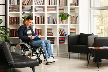 Young man in wheelchair choosing book in home library